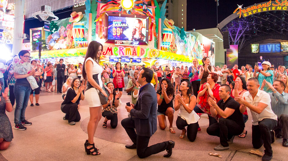 Man proposing during a lively flash mob performance on a crowded street, surrounded by cheering onlookers