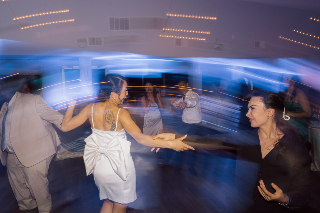 Guests dancing under dynamic lighting at a wedding reception, with motion blur capturing the energy and excitement on the dance floor.