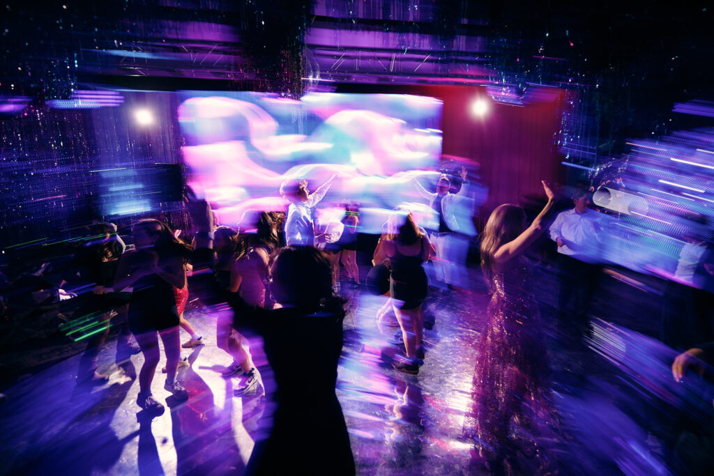 Guests dancing under vibrant purple and blue lights on a crowded dance floor, with motion blur capturing the energy and excitement of a NYX Events Bat Mitzvah party.