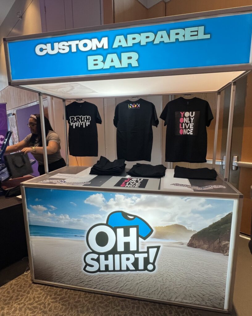 Two women smiling at an interactive mitzvah favors Baltimore booth with a custom apparel bar and heat press.