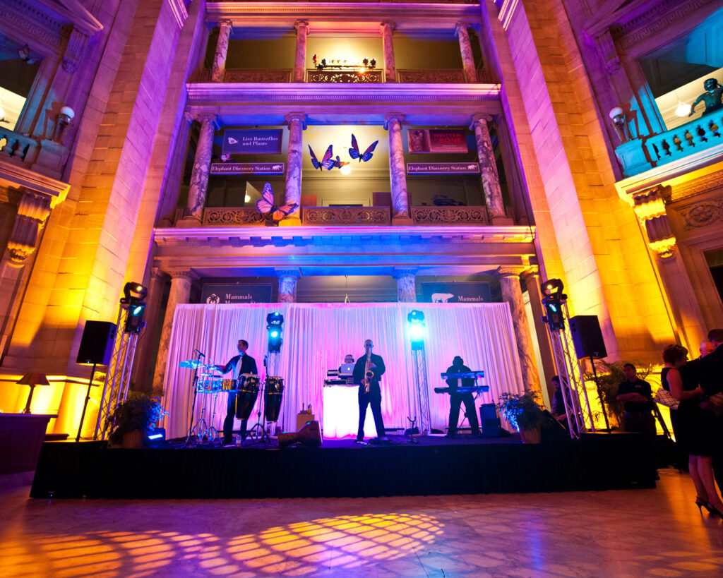 A high-energy dj with live musicians performing on a lit stage with saxophonist and percussionists at a gala.