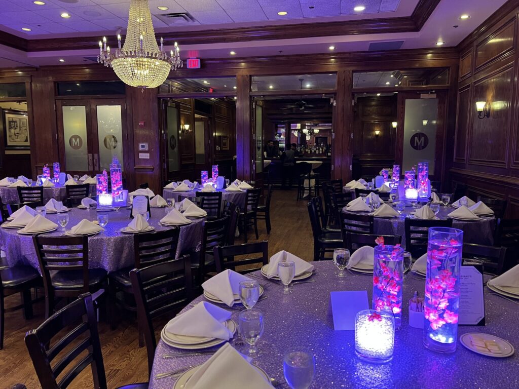 Pink flowers submerged in illuminated glass cylinder centerpieces on silver-covered banquet tables.